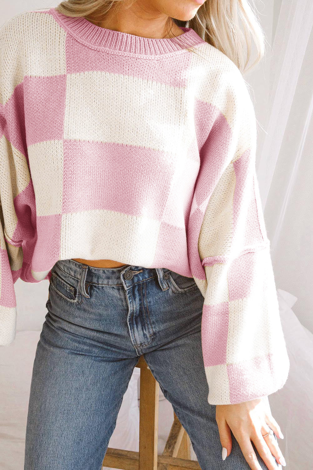 Model wearing a pink checkered bishop sleeve sweater paired with high-waisted jeans.