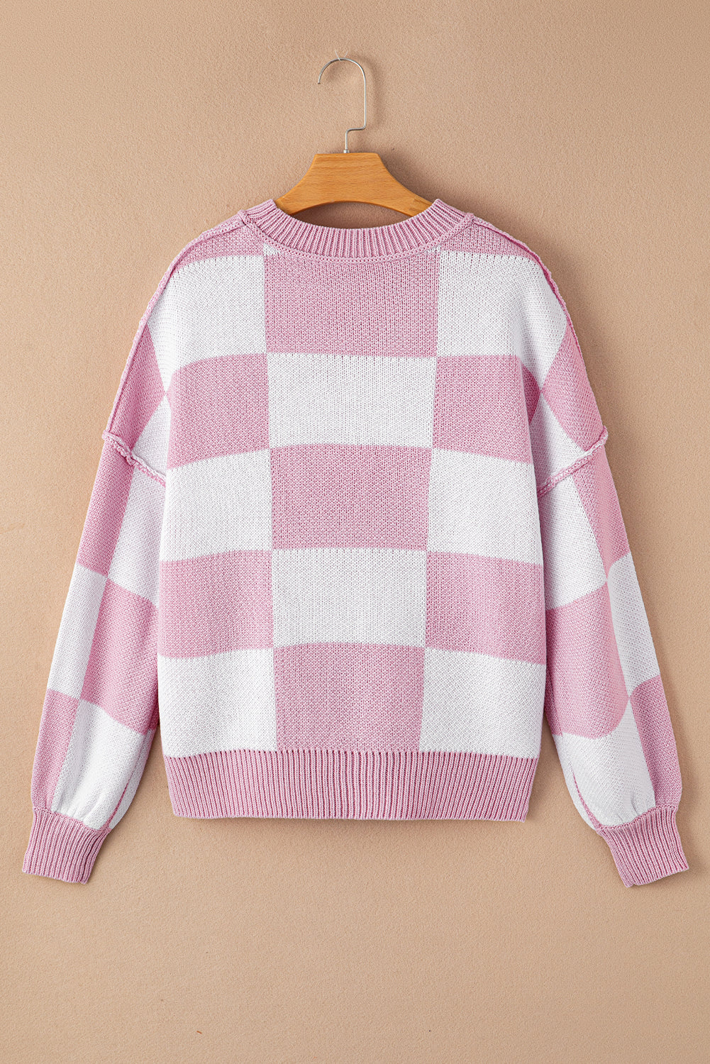 Back view of a pink checkered bishop sleeve sweater with a relaxed fit on a hanger.