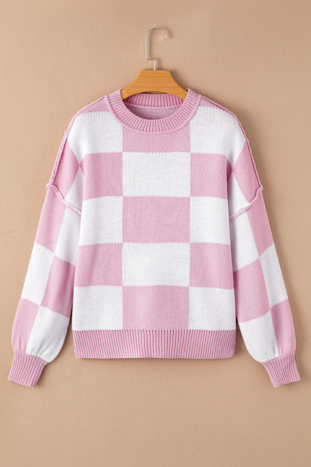 Pink checkered bishop sleeve sweater hanging on a beige background, showcasing its stylish design and soft fabric.